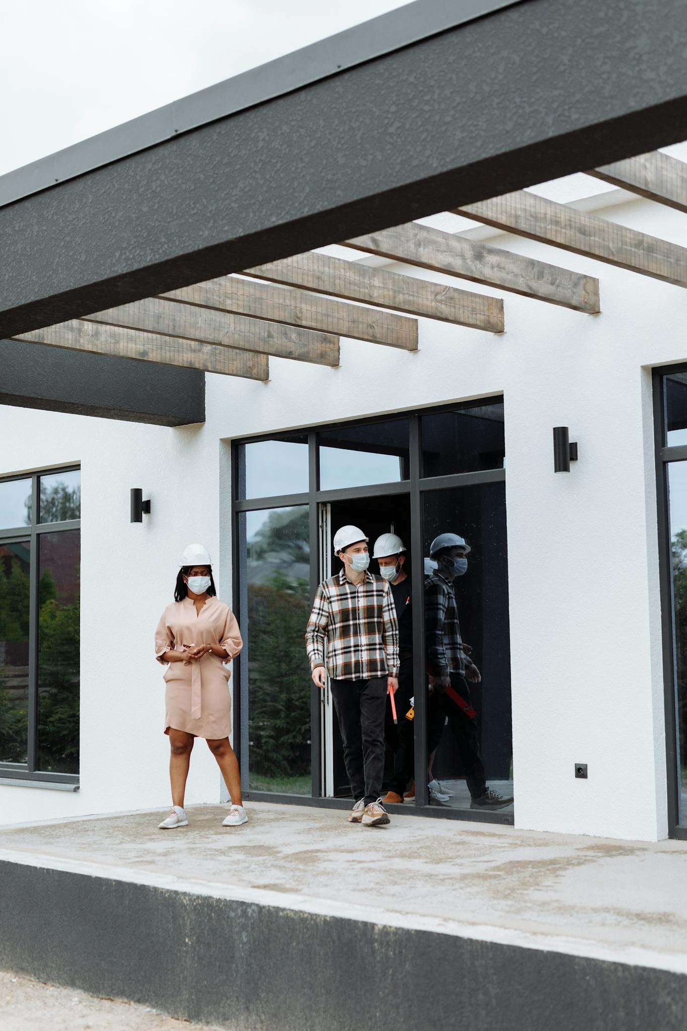Real estate agents discussing property during a site visit. Safety measures include masks and hard hats.